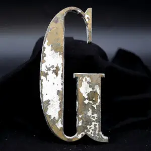 Overmalet messing-facadebogstav “G” med rå patina, afskallet maling og originale gevindstænger.