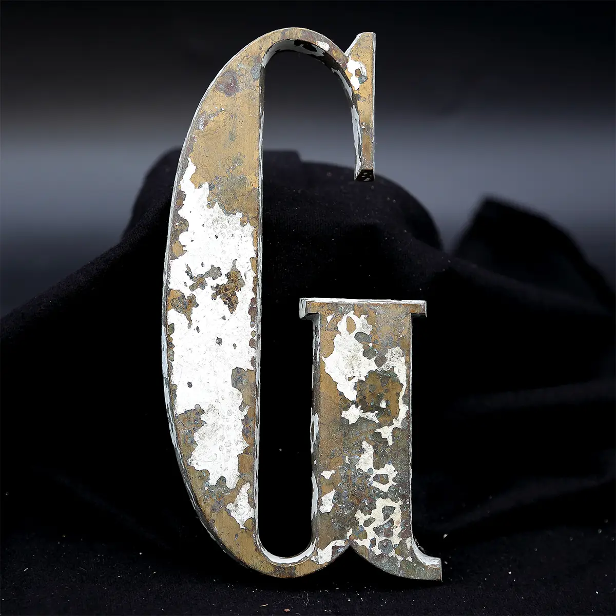 Overmalet messing-facadebogstav “G” med rå patina, afskallet maling og originale gevindstænger.