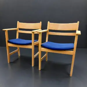 Sæt på to Hans J. Wegner armstole for Getama i lyst bøgetræ med blå uldhynder, original Getama-mærkning og proveniens fra Region Hovedstadens Genbrug og Donation.